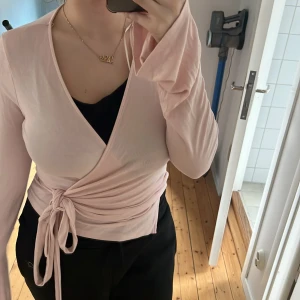 Ljusrosa omlottopp - Säljer en ljusrosa omlottopp med långa ärmar och knytning i midjan. Toppen har en v-ringad design. Är köpt på Gina tricot💗har knutit den fel på bilden insåg jag haha men ja! Sitter jätte fint och har aldrig använt