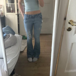 Blå bootcut jeans från Gap - Säljer ett par snygga blå bootcut jeans från Gap. De har en låg midja och slitna detaljer på framsidan som ger en trendig look. Perfekta för en avslappnad stil.Midjemått:39cm och innerbenslängden:81cm💕