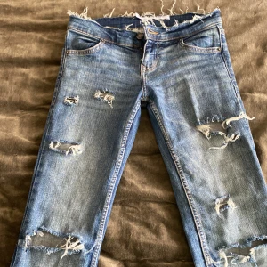 Blå slitna jeans - Säljer ett par blå jeans med slitningar och fransiga detaljer. De har en klassisk femficksdesign och är även bootcut ned till.💙 köpta för 600kr