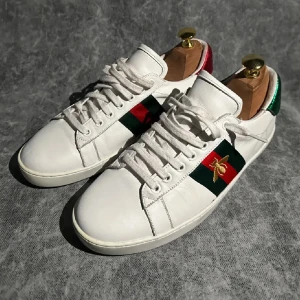 Gucci ace - Snygga vita sneakers från Gucci med ikoniska röd och grön rand på sidan och en guldbroderad bi på sidan av skon! Skorna är i storlek 41 och är i NYSKICK! nypris 9200kr mitt pris 1899kr