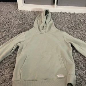 Grön hoodie från 157 - Säljer en stilren grön hoodie från 157. Den har en klassisk design med en stor ficka framtill och en bekväm huva. Perfekt för en avslappnad look.