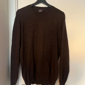 Brun tröja från Oscar Jacobson i 100% ull. - Säljer en stilren brun tröja från Oscar Jacobson, tillverkad i Italien. Tröjan har en klassisk design med långa ärmar och rund halsringning. Perfekt för en elegant och avslappnad look. Hör av dig vid fråga.