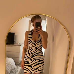 Zebramönstrad klänning från Gina Tricot - Snygg zebramönstrad klänning från Gina Tricot i svart och vitt. Klänningen har en djup v-ringning och knytband i nacken. Perfekt för en trendig look!