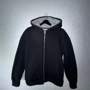 Produkt Teddy tröja - Stl L - Säljer en svart hoodie med dragkedja från Produkt. Den har en mysig fleecefodrad insida och en stor huva. Perfekt för kyliga dagar. Den har långa ärmar och två fickor framtill.