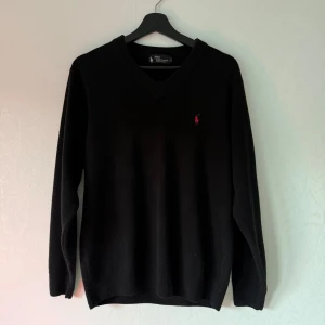 Ralph Lauren stickad tröja 100% cashmere! - L - Säljer en elegant svart kashmirtröja från Ralph Lauren med v-ringning och det ikoniska broderade logotypen i rött på bröstet. Tröjan har långa ärmar och är perfekt för en stilren look. Passar både till vardags och mer uppklädda tillfällen.
