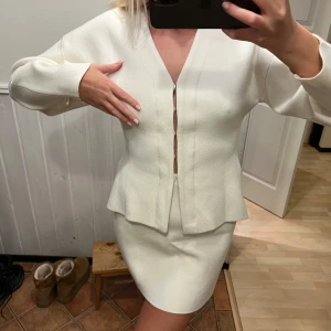 Vit kjol och kofta - Säljer en stilren vit kjol och matchande kofta. Koftan har långa ärmar och en elegant design med knappar framtill. Kjolen är kort och figurnära, perfekt för en chic look. Passar perfekt för vår och sommar!