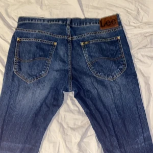 Blå jeans från Lee - Snygga blå jeans från Lee med klassisk femficksdesign och en bekväm passform. De har en knappgylf och är perfekta för en avslappnad stil. Märkeslogga på baksidan av midjan. Kontakta vid frågor.