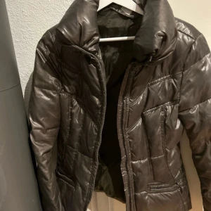 Militärgrön pufferjacka från Utility storlek S - Säljer en militärgrön pufferjacka från Utility med dragkedja framtill. Jackan har en hög krage och är perfekt för kyligare dagar. Den är stilren och enkel att matcha med olika outfits. Storlek S. 70% dun 30% fjäder