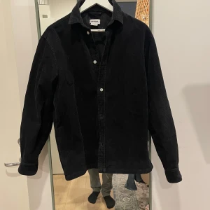 Svart manchester overshirt från Weekday - Snygg svart overshirt i manchester från Weekday. Perfekt för lager-på-lager-stil med knappar framtill och klassisk krage. Passar både till vardags och mer avslappnade tillfällen. Använd som max 3 gånger för 3 år sedan när jag köpte den!