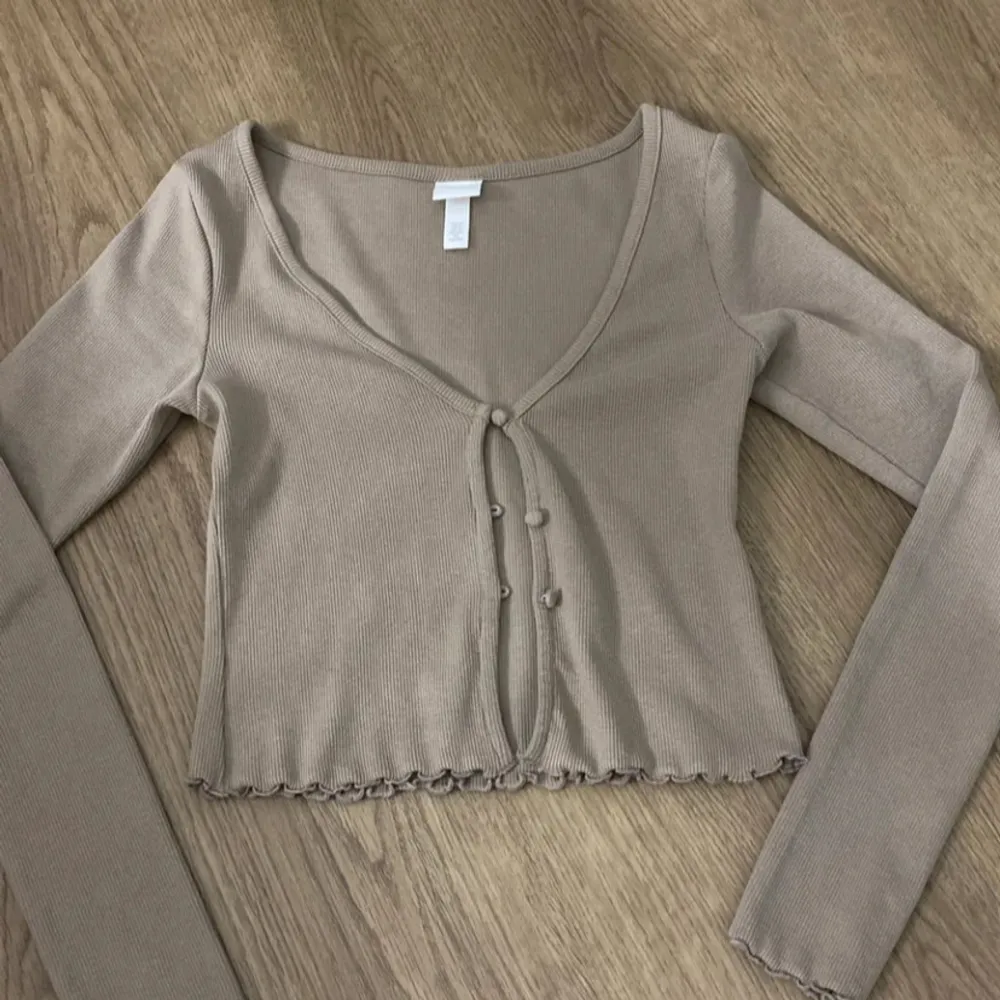 Beige tröja från HM i storlek XS med tre knappar och fina detaljer i ärmar och nertill.. Neuletakit & Villapaidat.
