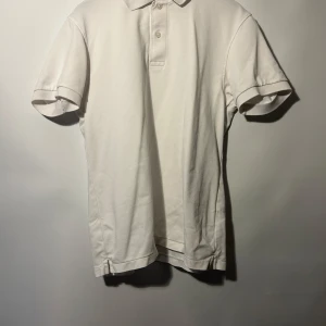 Vit pikétröja från Uniqlo - Säljer en klassisk vit pikétröja från Uniqlo. Tröjan har korta ärmar och en traditionell krage med knappar. Perfekt för en stilren och avslappnad look.