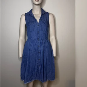Blå ärmlös jeansklänning från Bershka - Blå klänning från Bershka i denimstil. Tunn i materialet. Klänningen har knappar längs hela framsidan och två bröstfickor. 