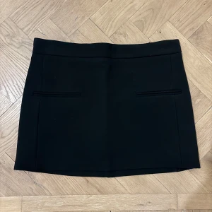 Svart minikjol från Zara - Svart minikjol från Zara med en stilren design. Kjolen har en dragkedja baktill och diskreta fickor framtill. Perfekt för en chic look. Endast använd ett fåtal gånger och är i mycket fint skick. Storlek XS.