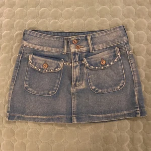 Jeanskjol med pärldetaljer - Snygg lågmidjad jeanskjol med diamantstuds och två fickor framtill. Säljer då den är lite kort på mig. Snygg till fest!