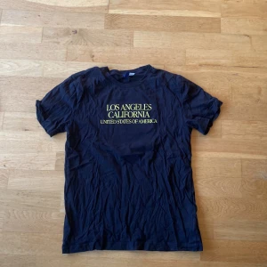 Svart t-shirt med Los Angeles-tryck - Säljer en svart t-shirt med tryck av 'Los Angeles California United States of America' på både fram- och baksidan. T-shirten har korta ärmar och är i bomull. Perfekt för en avslappnad stil.