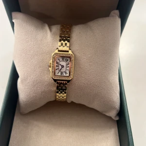 Guldfärgad rektangulär klocka - Elegant äkta guld klocka med rektangulär urtavla och romerska siffror. Klockan har en länkarmband i guld och en stilren design som passar perfekt för både vardag och speciella tillfällen.