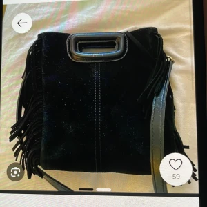 Svart axelväska med fransar - Snygg svart axelväska i mocka med coola fransar på sidorna. Väskan har en praktisk dragkedja och ett stilrent handtag i metall. Perfekt för att ge din outfit en edgy touch.