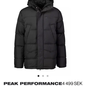 Marinblå dunjacka från Peak Performance - Säljer en stilren marinblå dunjacka från Peak Performance. Jackan har en praktisk dragkedja och knappar framtill, samt en justerbar huva. Perfekt för kalla dagar med sin vadderade design och flera fickor för extra förvaring. Använd 1 gång så nästan helt ny, den har inget slitage, nypris ca 4000 kr.
