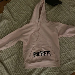 Rosa Bieber hoodie med anka - Säljer en rosa hoodie med texten 'Bieber' framtill och en stor gul anka med texten 'Changes' på baksidan. Hoodien har en stor ficka framtill och en justerbar huva. Perfekt för fans av Bieber! 💖