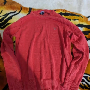 Röd bomullströja från GANT - Säljer en snygg röd tröja från GANT i 100% bomull. Tröjan har en broderad logotyp på bröstet och ribbstickade muddar vid ärmslut och nederkant. Perfekt för en stilren look!