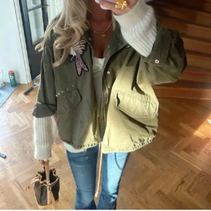 Olivgrön jacka med broderier - Snygg olivgrön jacka med coola broderier av fåglar och blommor. Jackan har en avslappnad passform med dragkedja och nitar på axlarna. Perfekt för en trendig look! Jackan är i storlek M och bilderna är lånade. Skulle kunna tänka mig att byta till en Storlek S eller för rätt pris. 💕💕