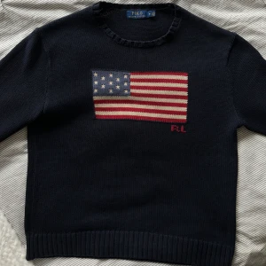 Marinblå stickad tröja från Polo Ralph Lauren - Snygg blå stickad tröja från Polo Ralph Lauren med den ikoniska amerikanska flaggan på bröstet. Tröjan har långa ärmar och ribbade muddar vid ärmslut. Trendar på TikTok är är näst intil omöjlig att få tag på. Ligger på över 6 000 nypris. Ändast seriösa köpare! Skriv om du vill ha fler bilder🔥 //Calle 