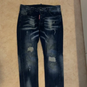 Blå jeans från Dsquared2 - Snygga blå jeans från Dsquared2 med slitna detaljer och en klassisk femficksdesign. Jeansen har en straight passform och är perfekta för en avslappnad stil. Märkeslappen i läder sitter baktill i midjan.