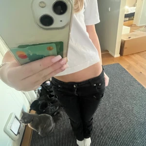 Svarta bootcut jeans med hål i - Snygga svarta bootcut jeans med slitna detaljer på knäna. De har en låg midja och klassisk femficksdesign. Perfekta för en avslappnad stil. Midjemått 35/36cm och innerbenslängden 75/76