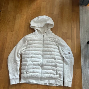 Vit jacka med huva från Moncler - Säljer en stilren vit jacka från Moncler med huva och dragkedja. Snören medföljer och mer bilder kan skickas. 