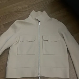 Beige jacka med dragkedja - Säljer en stilren beige jacka med dragkedja och två stora fickor framtill. Jackan har långa ärmar och en hög krage, perfekt för kyligare dagar. Materialet är mjuk sitter bekväm, bra kvalitet. Passar bra till både vardag och mer uppklädda tillfällen💕😇