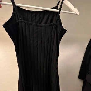 Svart ribbad klänning - Snygg svart ribbad klänning med smala axelband och rynkdetalj framtill. Perfekt för en stilren look.