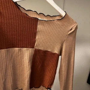 Ribbad långärmad topp i beige och brun - Snygg ribbad topp med lång ärm i en mix av beige och brun. Den har en unik design med vågig kant vid halsen och nederkanten. Perfekt för en trendig look.