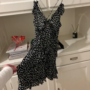 Svart prickig klänning med volangdetaljer - Säljer en söt svart klänning med vita prickar och volangdetaljer. Klänningen har smala axelband och en luftig passform, perfekt för varma dagar. Den är kort och har en lekfull design som ger en ungdomlig känsla. Perfekt för sommarens alla tillfällen! Från Zara i storlek XS.