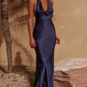 Mörkblå långklänning med öppen rygg - Elegant mörkblå långklänning i satin med djup v-ringning och öppen rygg. Klänningen har en smickrande passform och knytband i nacken. Perfekt för en glamorös kväll. Klänningen är från Zara! 