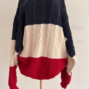 Randig stickad tröja från American Sports Wear - Säljer en snygg stickad tröja från American Sports Wear i randigt mönster med färgerna blå, creme och röd. Tröjan har en klassisk design med långa ärmar och rund halsringning. Perfekt för kyligare dagar! Stl M men passar även L.