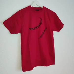 Röd t-shirt från James Harvest - Snygg röd t-shirt från James Harvest med ett unikt svart mönster på framsidan. Perfekt för en avslappnad stil. Tillverkad i ett bekvämt material som passar bra till vardags.