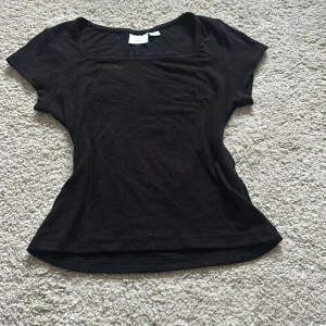 Svart topp från Gina Tricot - Säljer en stilren svart topp från Gina Tricot i storlek 146/152. Toppen har en enkel design med korta ärmar och rund halsringning. Perfekt för en avslappnad look.
