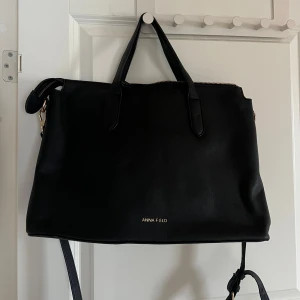 Svart axelväska från Anna Field - Snygg och stilren svart axelväska från Anna Field. Väskan är i skinnimitation och har en praktisk dragkedja upptill. Perfekt för både vardag och fest, med gott om plats för alla dina nödvändigheter. Den har två handtag och en justerbar axelrem för bekväm användning.