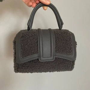 Handväska - Grå handväska i nyskick utan några defekter. Den kommer med ett axelband som man kan sätta på. Säljer för att den inte kommer till användning.