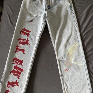 Unika jeans med tryck - Säljer ett par unika jeans med coolt tryck av vita duvor och röd text längs benen. De är i en ljus tvätt och har en straight passform. Perfekta för att sticka ut i mängden! 🕊️