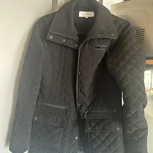Jacka  - Calvin Klein svart quiltad jacka (S) Säljer en snygg och stilren svart jacka från Calvin Klein, storlek medium. Perfekt för höst/vinter med två dragkedjefickor och två större fickor framtill. Bra skick, sparsamt använd. Pris kan diskuteras vid