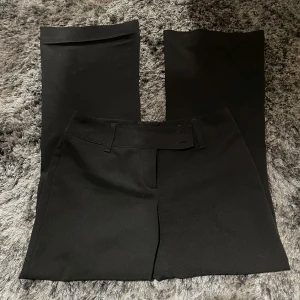 Svarta kostymbyxor från KappAhl - Säljer ett par stilrena svarta Lågmidjade kostymbyxor från KappAhl i storlek 38. Byxorna har en klassisk design med rak passform och är tillverkade i polyester och elastan för en bekväm känsla. Perfekta för både kontoret och festligare tillfällen!