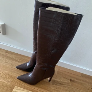 Stövlar från NA-KD - Säljer ett par bruna stövlar i krokodilmönster från NA-KD. Aldrig använda, endast provade. Storlek 38. Nypris 899