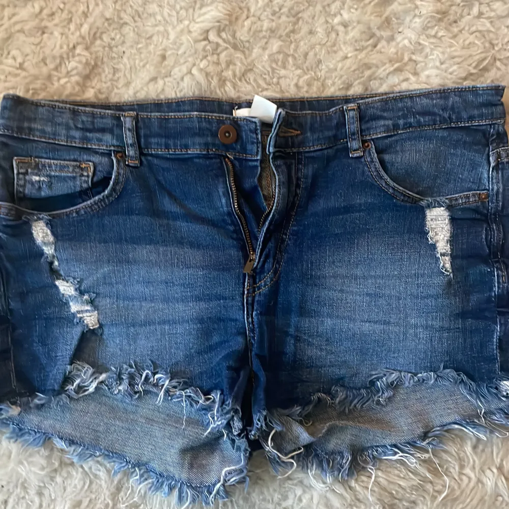 Säljer ett par coola blå jeansshorts i storlek 40.De har snygga slitningar fram och bak samt fransiga kanter för en avslappnad look. Perfekta för sommardagar eller festivaler! 🕶️. Shorts.