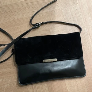 Svart axelväska från Wera - Snygg svart axelväska från Wera i både skinn och mocka. Perfekt för en kväll ute eller en dag på stan. Väskan har en justerbar axelrem och en stilren design med en metallplatta framtill. Passar till alla outfits är lite repig på märket men det skulle jag inte säga att man tänker på:)