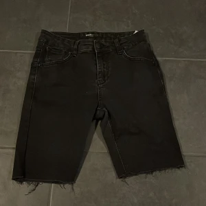 Svarta jeansshorts med rå kant - Säljer ett par svarta jeansshorts i bra skick. De har en rå kant nertill för en cool look och är perfekta för sommarens alla äventyr. Shortsen har en normal passform och är midwaist. De har klassiska fem fickor och stängs med dragkedja och knapp.