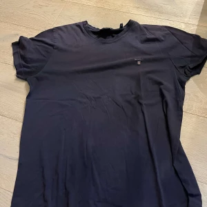 Svart t-shirt från GANT - Säljer en stilren svart t-shirt från GANT i storlek L. Den är kortärmad och har en liten broderad logga på bröstet. Perfekt för både vardag och fest. T-shirten är i bra skick och gjord av mjuk bomull.