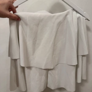 Vit volangkjol - Säljer en stilren vit kort volangkjol. Perfekt för sommarens fester eller en avslappnad dag ute. Kjolen har en lös passform som ger en luftig känsla. Lappen har åkt av men den är i storlek xs. Går att använda som tubtopp också🌟