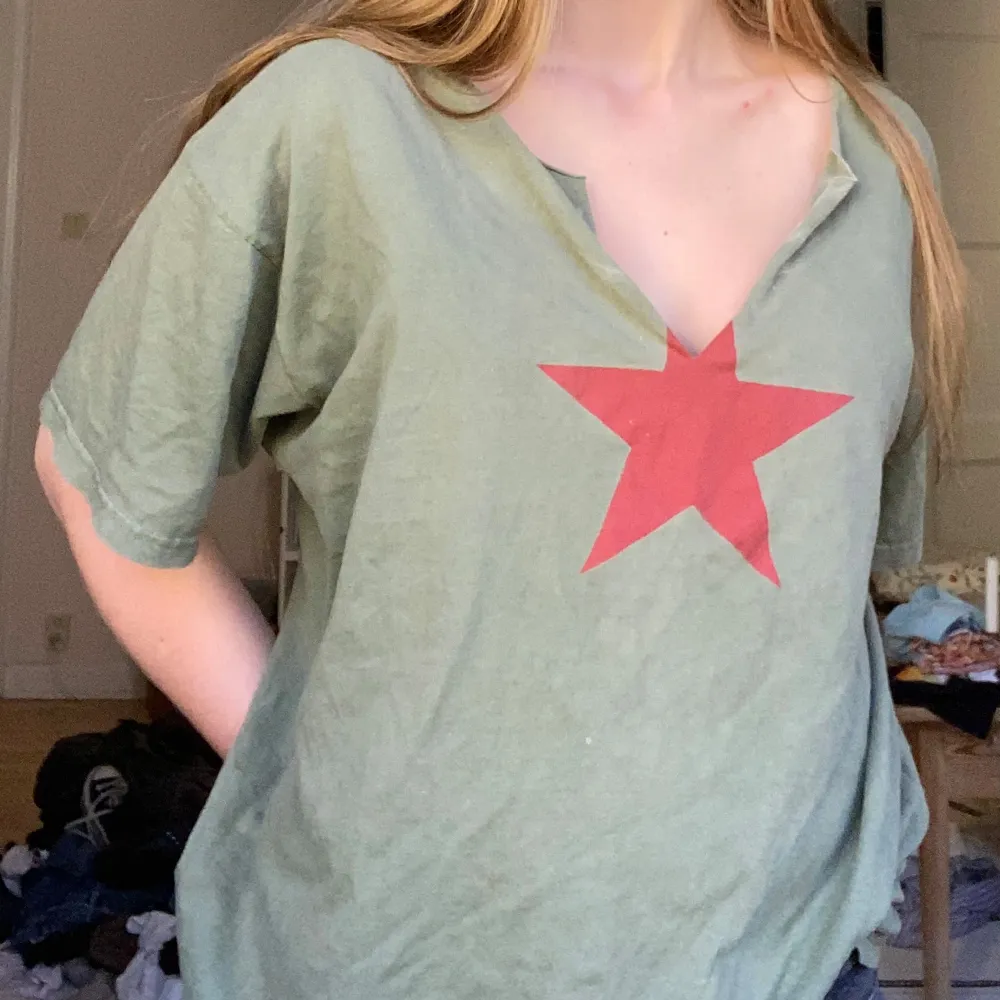 Säljer en grön t-shirt med en stor röd stjärna på bröstet. T-shirten har en avslappnad passform och är kortärmad med en v-ringad hals. Perfekt för en casual look eller som statement-plagg. Passar bra till jeans eller shorts!. T-shirts.