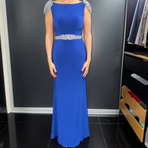 Blå långklänning med pärldetaljer - Elegant blå långklänning med vackra pärldetaljer på axlar och midja. Klänningen har en öppen rygg och är perfekt för festliga tillfällen. Den är ärmlös och har en figurnära passform som framhäver silhuetten.
